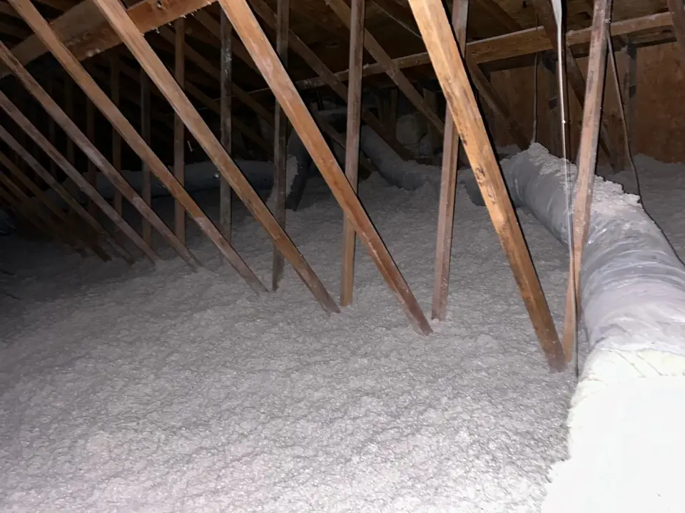 Fresh blown-in cellulose across an attic floor, reaching the insulated ducts