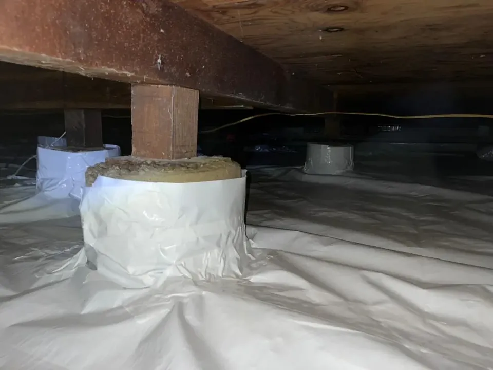 Crawl space covered with a white vapor barrier wrapped around the piers