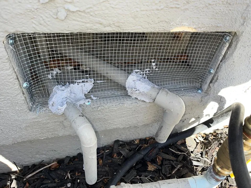 Foundation vent covered with screwed-in steel mesh, the two pipes through it sealed with putty