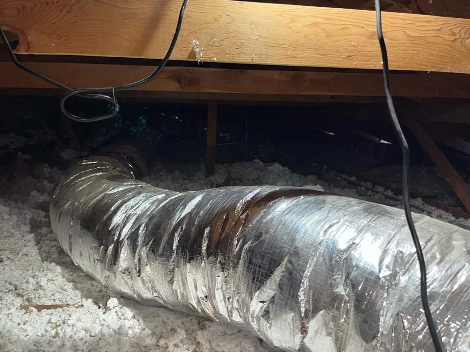 New silver flexible insulated duct run over fresh insulation in an attic